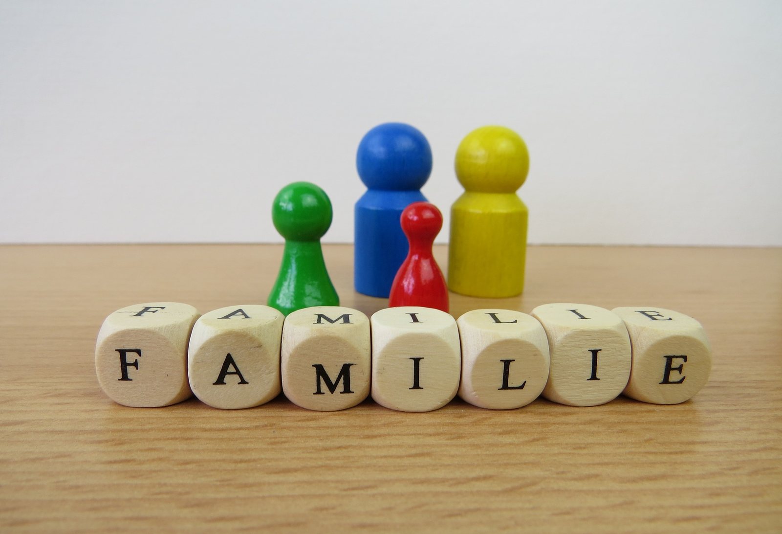 Bunte Spielfiguren hinter Holzwürfeln, die das Wort FAMILIE bilden